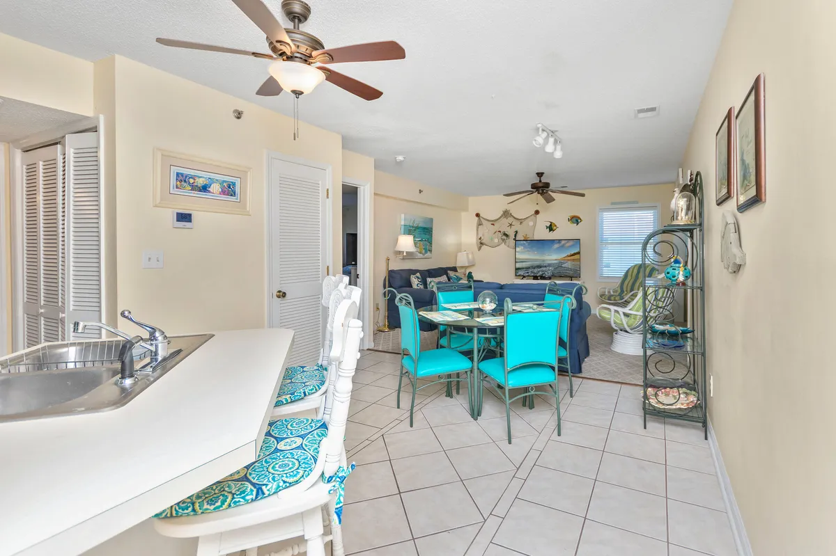 A bright, open-concept living and dining area seamlessly connects the kitchen bar, dining table, and a cozy sofa area. Decorative wall art and abundant natural light create a cheerful and welcoming atmosphere, ideal for group gatherings and relaxing afternoons.