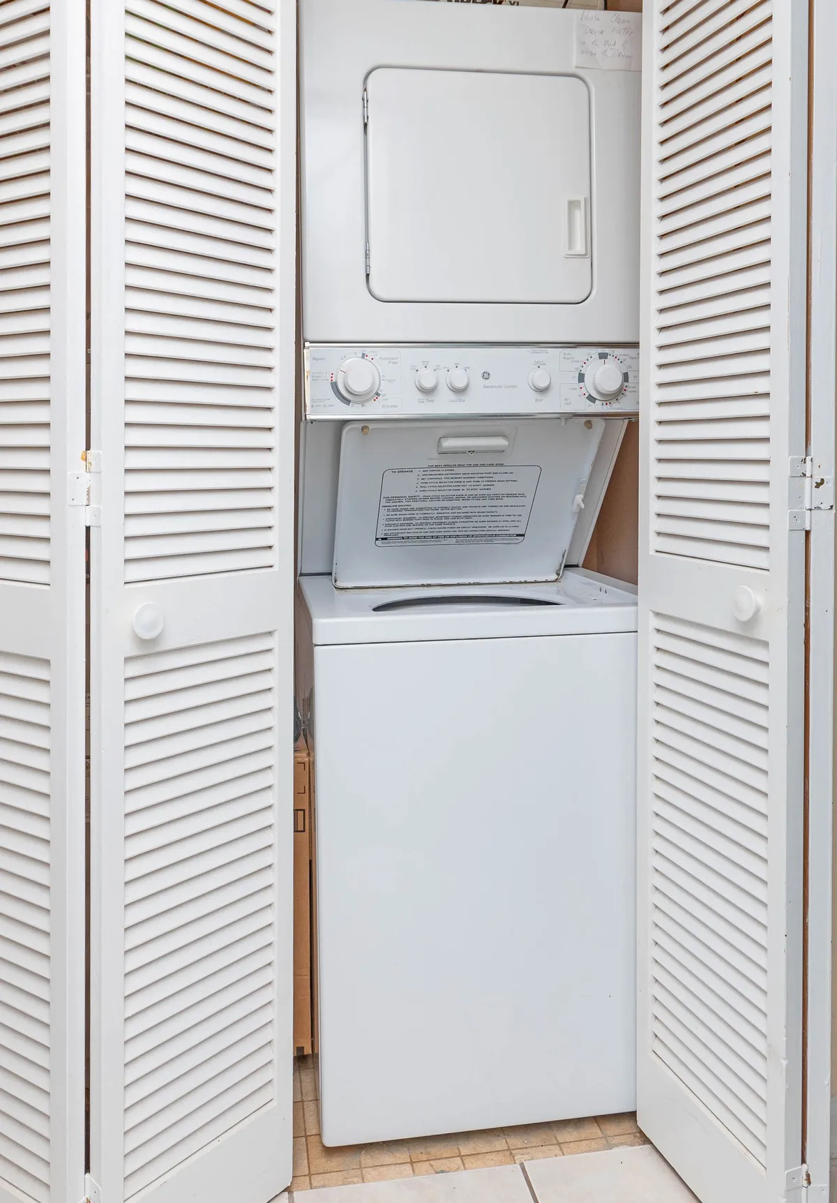 This image displays a neatly organized laundry area featuring a stacked washer and dryer with white louvered doors, emphasizing the convenience of in-unit laundry amenities.