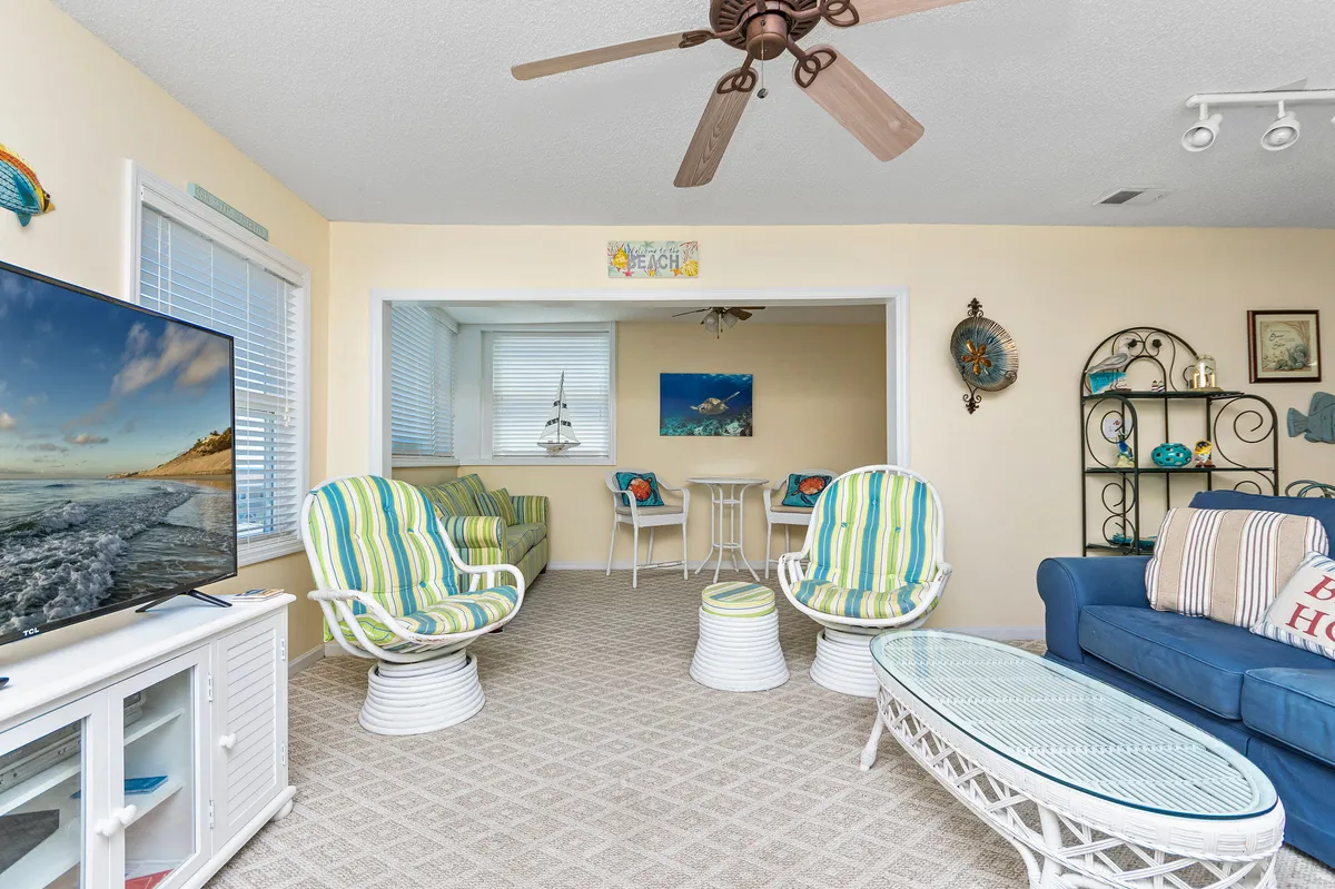 A cheerful living area featuring colorful seating, a coffee table, and a television, with decorative wall art adding to the inviting ambiance. The setup suggests a space perfect for relaxing with friends or savoring morning coffee while possibly enjoying glimpses of the outdoors.