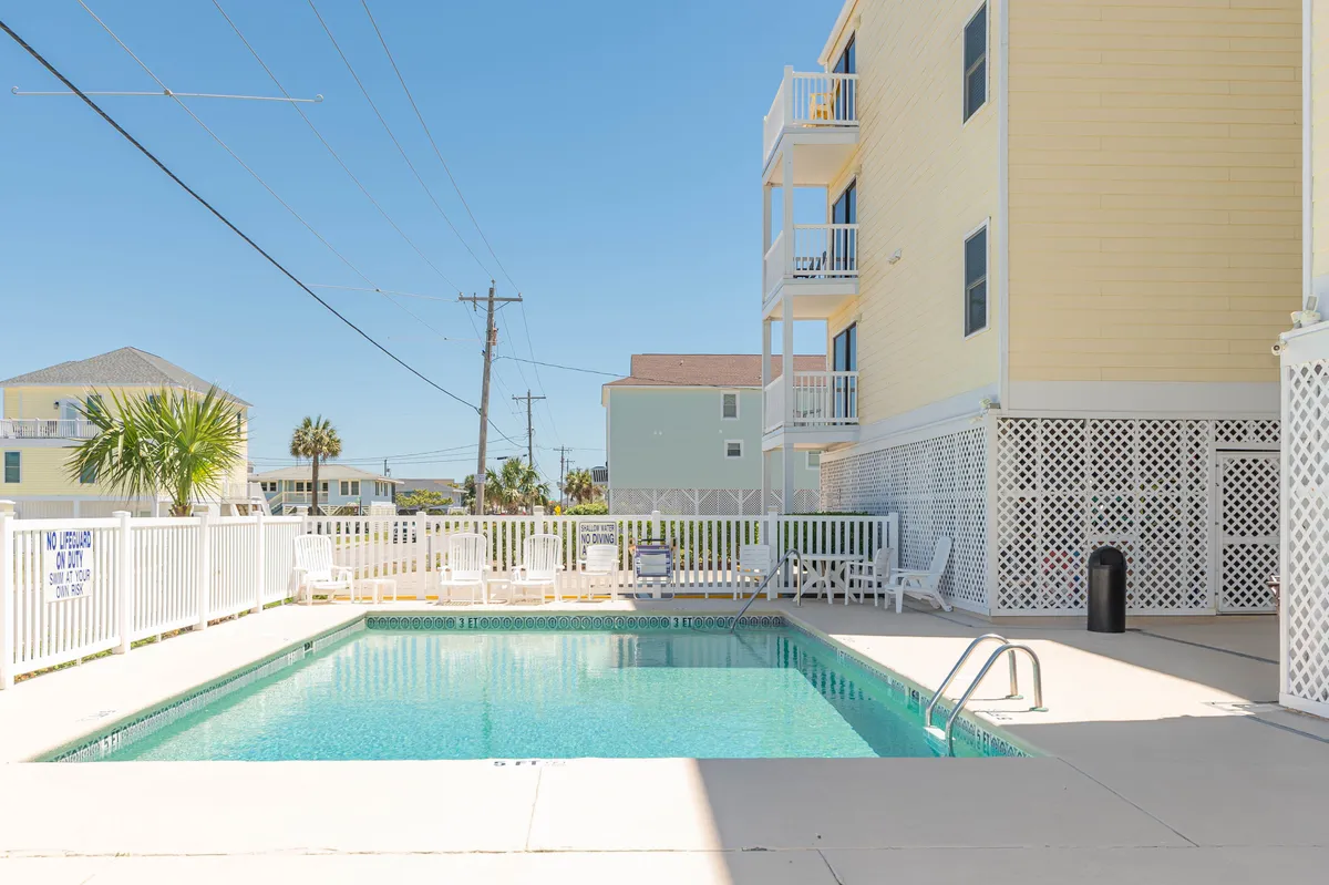 The sparkling community swimming pool is surrounded by inviting lounge chairs and set against the backdrop of the property buildings, creating a tranquil spot for both families and couples to unwind.