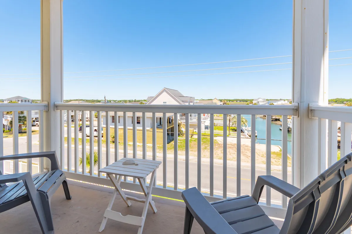 An inviting balcony scene with chairs and a small table overlooks tranquil water and nearby homes. The view suggests proximity to outdoor recreation and opportunities for relaxing family moments between adventures.