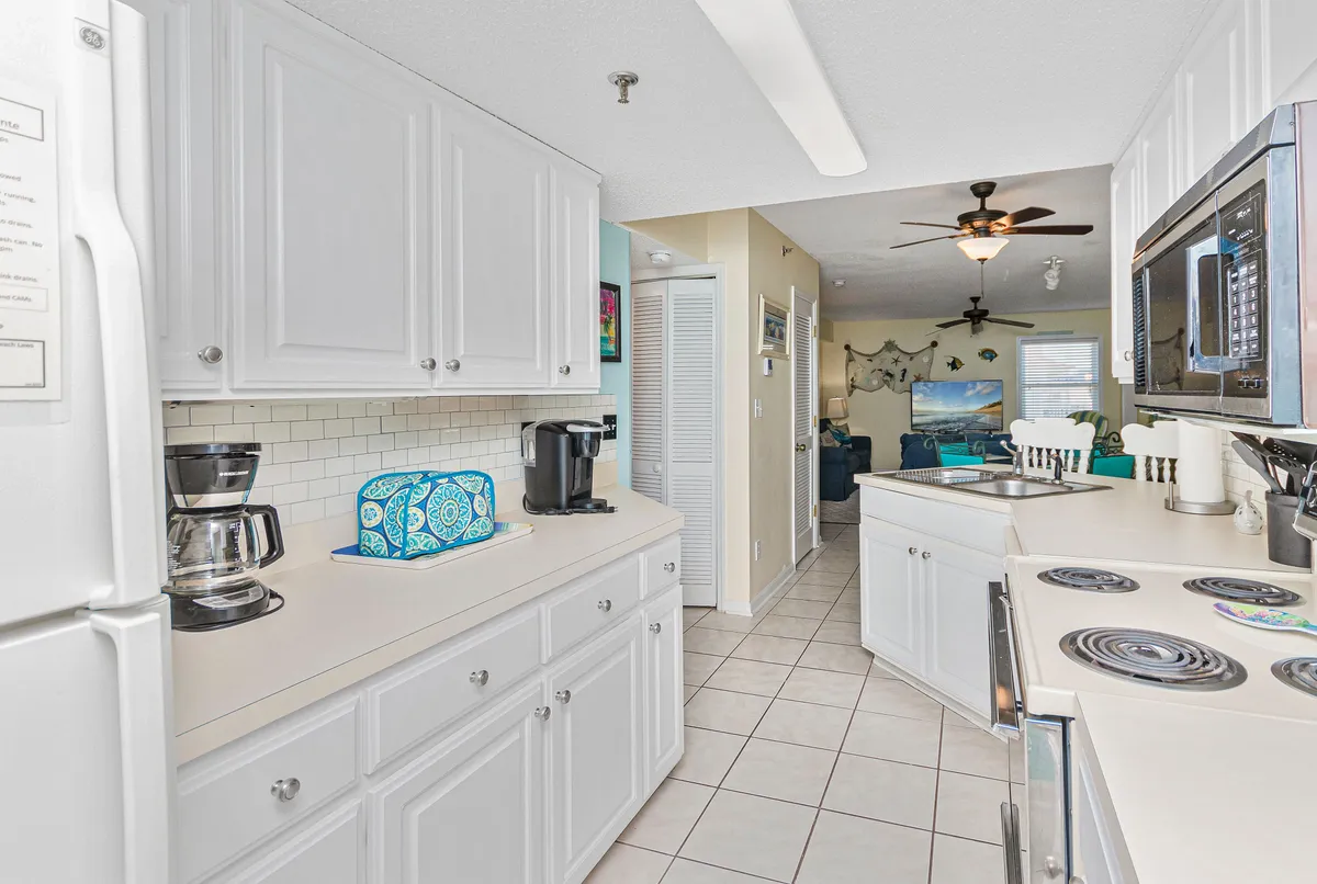 A cheerful kitchen scene with white cabinetry, a coffee maker, and a colorful storage container, all opening into a bright living area—perfect for easy meal prep and relaxed socializing.